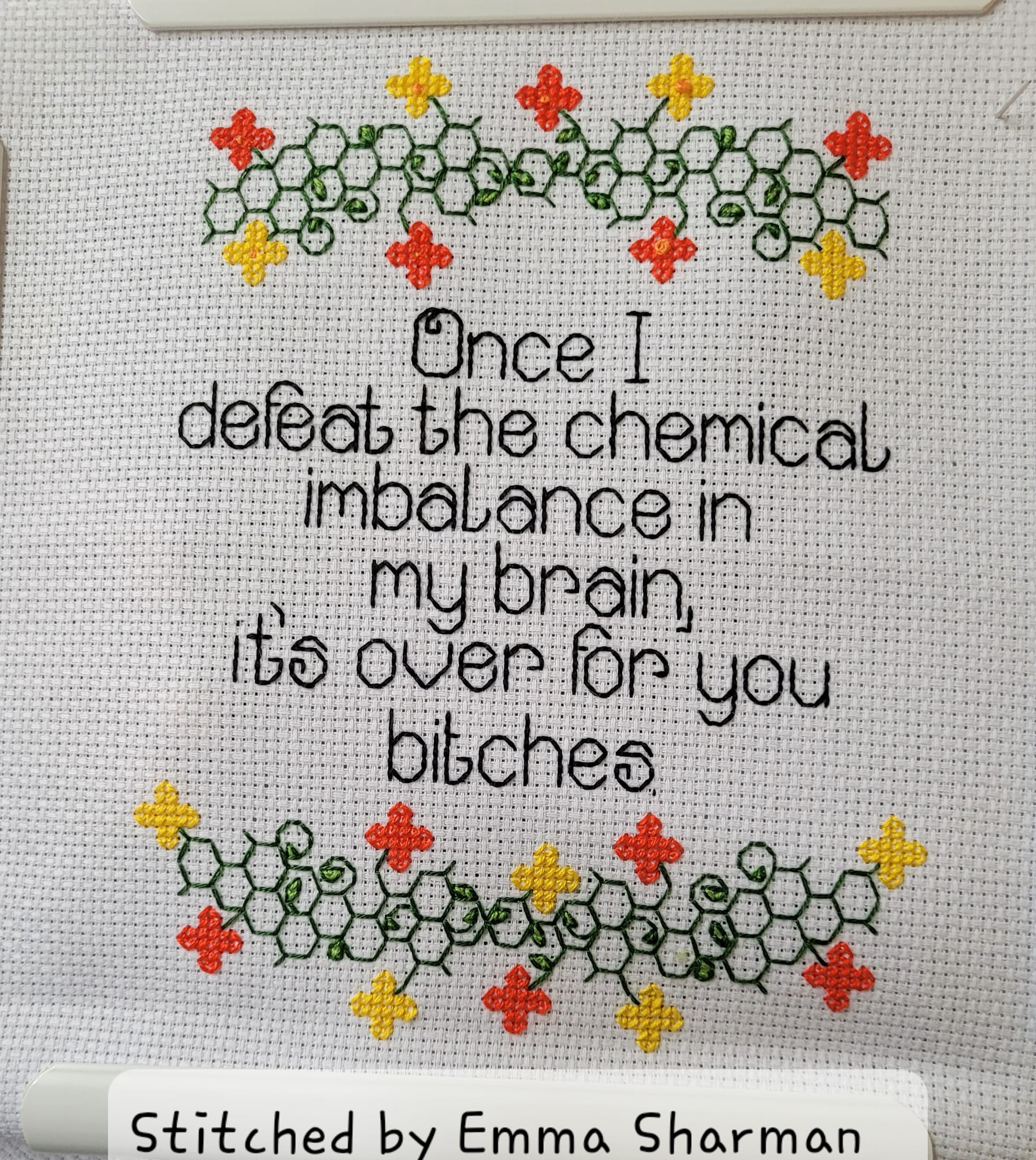 [Image description: Photo of a cross stitch. There is a floral boarder with orange and yellow flowers and the stems are designed to look like molecules. Back stitched text in black reads 'Once I defeat the chemical imbalance in my brain, it's over for you bitches.' There's also a digital sticker that says 'Stitched by Emma Sharman'. End description.]